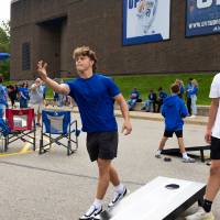 Students play cornhole game in tailgate parking lot.